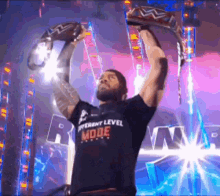 a man wearing a different level mode shirt is holding a wrestling belt in the air