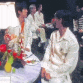 a group of people are sitting at a table with flowers and drinks .