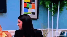 a woman is sitting in front of a blue wall with a smp logo on the bottom right