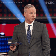 a man in a suit and tie is holding a piece of paper with the words family feud canada on it