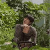 a man is sitting in front of a laptop in a greenhouse with his mouth open .