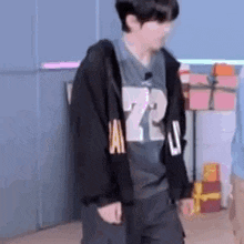 a man wearing a black hoodie and a gray shirt with the number 72 on it is standing in a room .