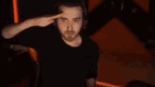 a man wearing headphones is saluting while standing in front of a computer screen .