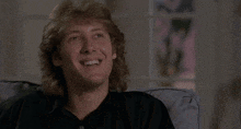 a man with blonde hair is smiling while sitting in a chair