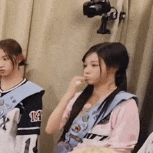a girl is brushing her teeth in front of a camera while another girl stands behind her .