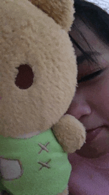 a woman is holding a stuffed animal with a green shirt with x stitched on it