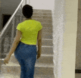a woman in a yellow shirt and jeans is walking up the stairs .