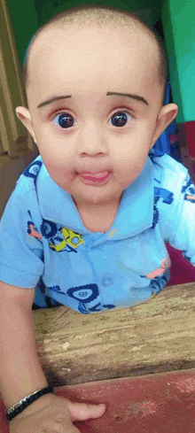 a baby wearing a blue shirt with cars on it sticking his tongue out