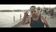 a man in a black tank top is standing on a beach making a funny face .