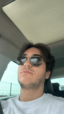 a man wearing sunglasses sits in a car with the sunroof open