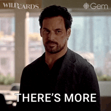 a man with a beard is standing in front of a window and says there 's more