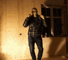 a man wearing glasses and a plaid shirt is standing in front of a wooden wall