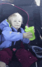 a child in a car seat holds a green cup