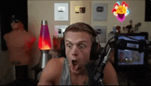 a man wearing headphones looks surprised in front of a microphone and a lava lamp