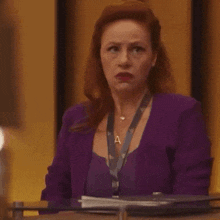 a woman in a purple suit is making a surprised face while sitting at a table .