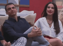 a man and a woman are sitting next to each other on a couch and holding hands .