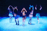 a group of women are dancing on a stage in blue lights
