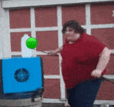 a fat man in a red shirt is throwing a balloon in a target .