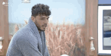 a man with curly hair and a beard is wearing a blue sweater and a blue towel around his neck .