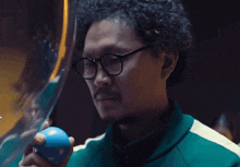 a man with glasses holds a blue ball in his hand