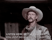 a man in a cowboy hat is standing in a dark room .