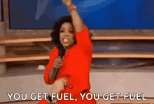 a woman in a red dress is holding a microphone and saying `` you get fuel you get fuel '' .