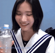 a girl in a sailor uniform holds a plastic bottle in her hand