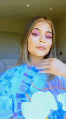 a woman wearing a blue tie dye shirt has pink eyeshadow on her eyes