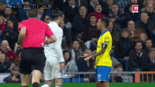 a soccer player wearing a yellow jersey with the letter e on it talks to a referee