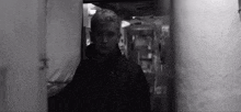 a black and white photo of a man standing in a narrow hallway .