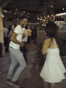 a man in a white shirt is dancing with a girl in a white dress