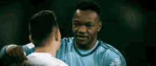 a man in a blue shirt is hugging another man in a white shirt on a soccer field .