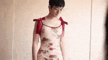 a young man is wearing a floral dress with red bows on the shoulder straps .