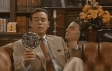 a man in a suit and tie is sitting on a couch holding a mirror ..