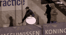 a man playing a drum in front of a sign that says koningin