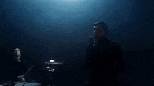 a man playing drums in a dark room with smoke behind him