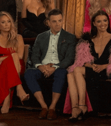 a group of women are sitting on a couch with one wearing a pink feathered coat