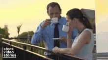 a man and a woman are sitting on a balcony drinking coffee .