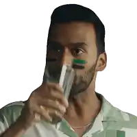 a man with green and black paint on his face is drinking from a glass