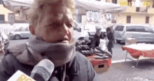 a woman wearing a scarf is talking into a microphone while standing in front of a market .