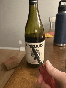 a bottle of linquist syrah is being cut with a knife