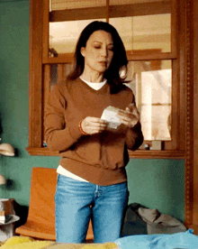 a woman in a brown sweater and blue jeans holds a piece of paper