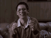 a young man with glasses is sitting on a couch eating a sandwich .