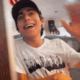 a young man wearing a hat and a white t-shirt is laughing .