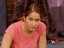 a woman in a pink shirt is making a funny face while sitting on the floor .