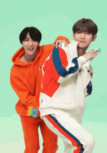 a man in an orange hoodie is standing next to a man in a white jacket