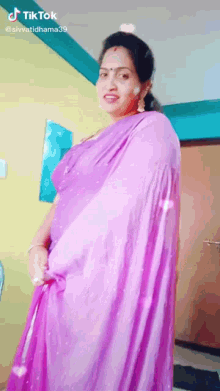 a woman in a purple saree is standing in a room and smiling .