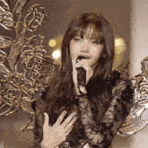 a woman singing into a microphone in front of a statue