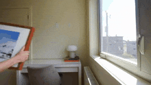 a person is holding a picture frame in front of a window