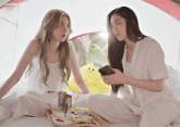 two women are sitting on a bed and one is holding a cell phone with the watermark lingeriecoffee